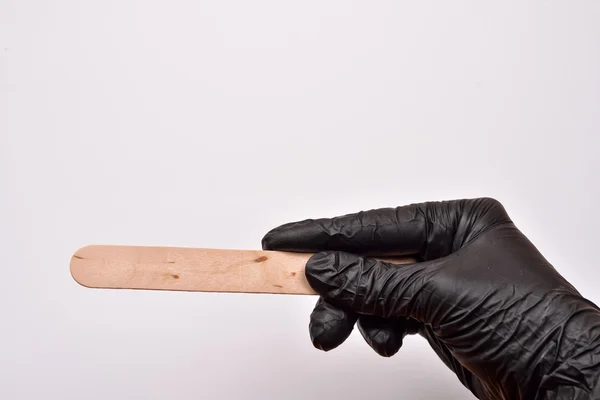 Una mano esteticista con guante negro sosteniendo una espátula para cera, p — Foto de Stock