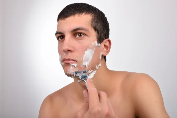 Bello giovane uomo con un sacco di crema da barba sul viso prepar — Foto Stock