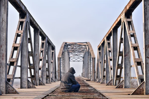 Sad teenager in depression sitting on the bridge at the sunset. — Stock Photo, Image