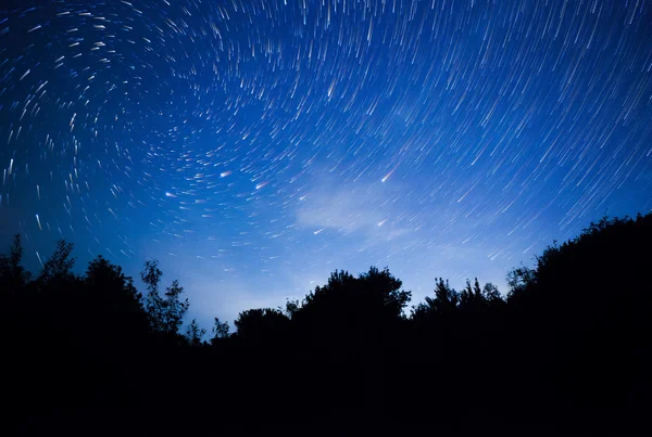 Hermoso cielo nocturno, senderos espirales de estrellas y el bosque — Foto de Stock