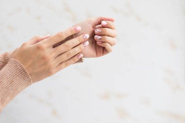 Açık arkaplanda Pastel bej manikür. Manikürlü tırnaklar ve fotokopi alanı olan yumuşak eller. Kadınların elleri kalın süveter içinde.