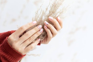 Açık arkaplanda Pastel bej manikür. Manikürlü tırnaklar ve fotokopi alanı olan yumuşak eller. Kadınların elleri kalın süveter içinde.