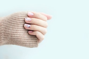 Açık arkaplanda Pastel bej manikür. Manikürlü tırnaklar ve fotokopi alanı olan yumuşak eller. Kadınların elleri kalın süveter içinde.