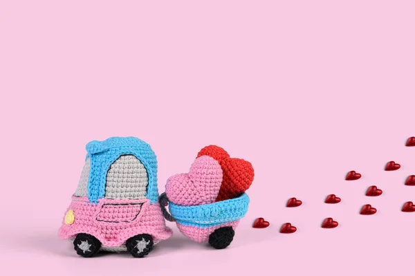 A knitted toy car with a trailer carries two hearts. Concept for the day of lovers or honeymoon trip.