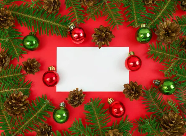 Kırmızı arka planda köknar ağacı dalları, koniler ve takılar olan bir kartpostal. Fotokopi alanı olan düz bir Noel.