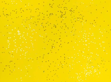 Sarı arka planda parlayan konfeti yıldızları.