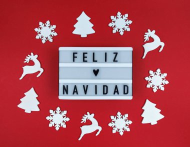 Feliz Navidad 'ın deyimiyle ışıklı kutu, İspanyol Mutlu Noeller kırmızı arka planda tahta oyuncaklarla.