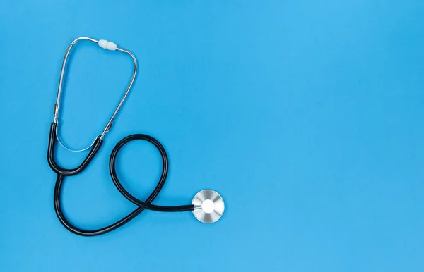 Black stethoscope on blue background. Simple flat lay with copy space. — Stock Photo, Image