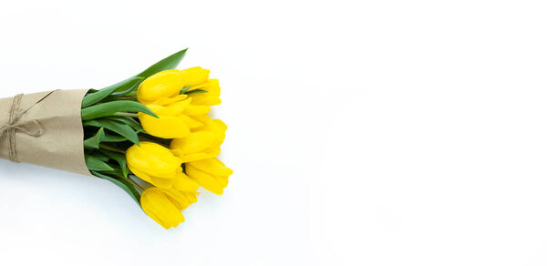Bouquet of yellow tulips wrapped in craft paper on a white background with copy space.