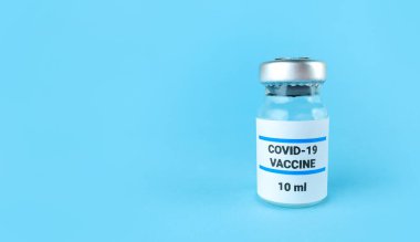 Mavi zemin üzerinde covid 19 aşısı olan ilaç şişesi..