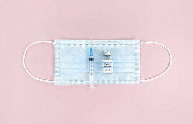 Şırınga, ilaç şişesi ve pembe arka planda yüz maskesi..