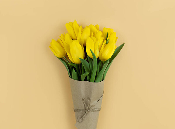 Bouquet of yellow tulips wrapped in craft paper on a beige background.