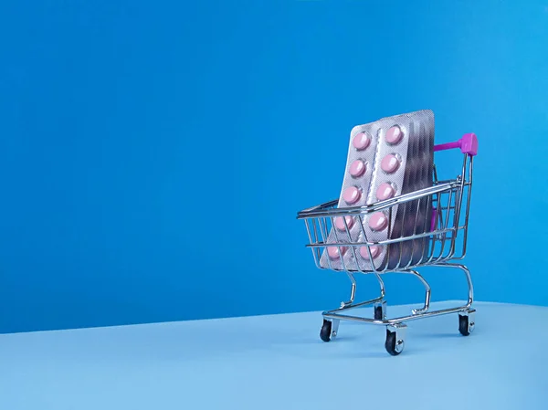 Süpermarket tramvayında pembe tabletlerin kabarcıkları mavi bir zemin üzerinde eğik gökyüzü çizgisi ve kopyalama alanı ile.