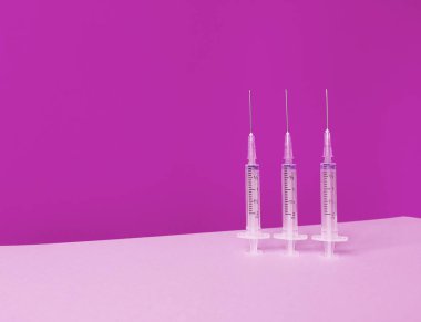 Pembe arka planda üç şırınga. Moda silueti ve kopyalama alanı var..