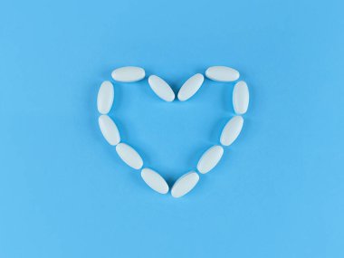 Mavi zemin üzerinde beyaz tabletlerden yapılmış kalp şekli.