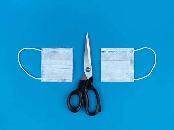 Medical disposable face mask cut in half and scissors on blue background.