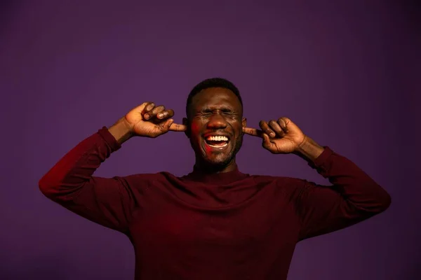 Black man with index fingers in ears and eyes closed with anguished expression. Front view. Medium shot. Isolated background.