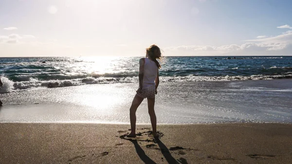 子供の日当たりの良いビーチの砂の上に立って 後ろの景色 水の上の地平線 ロングショット — ストック写真