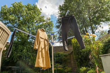 Coat and pants hang drying outdoors in sunny lush green backyard. Low angle view. Wide shot.  clipart