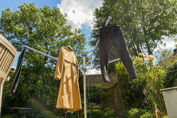 Coat and pants hang drying outdoors in sunny lush green backyard. Low angle view. Wide shot. 