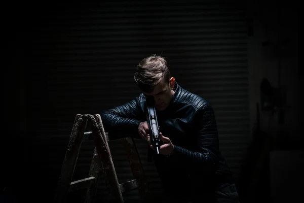 Młody człowiek w ciemnym garażu wskazując broń — Zdjęcie stockowe