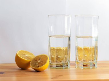 Tahta masadaki su bardağının arkasındaki limon. Beyaz arka plan. Boşluğu kopyala