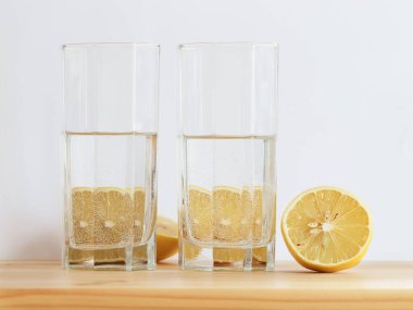 Tahta masadaki su bardağının arkasındaki limon. Beyaz arkaplan.