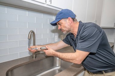 Modern evdeki mutfak lavabosu için sprey musluk üzerinde çalışan bir tesisatçı.