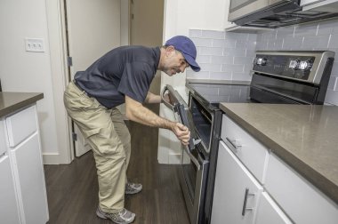 Cihaz teknisyeni modern bir aralıkta fırın kapısını tamir ediyor.