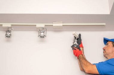 Elektrikçi tavandan bir ray aydınlatma armatürü çıkarıyor.