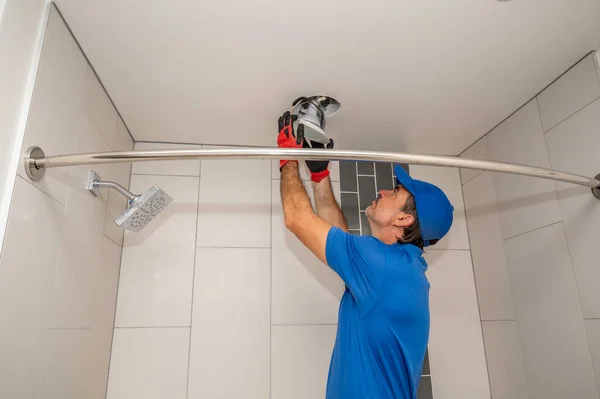 電気技師は浴室の天井の軽い据え付け品で働く ロイヤリティフリーのストック写真