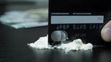 Adam banka kartıyla kokain yolu yapıyor. Uyuşturucu bağımlısı el, siyah arkaplanlı beyaz uyuşturucu barutunu tamir ediyor. Beyaz toz kartonla düzenlenir. Bağımlılık ve madde bağımlılığı kavramı