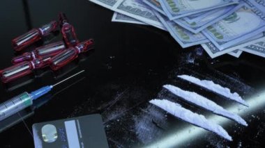 Beyaz uyuşturucu barutu, siyah arka planda ABD doları banknotları, şırıngalar ve uyuşturucu maddeleriyle samandan emilir. Bağımlı adam uyuşturucu kullanmaya hazırlanıyor. Siyah masada beyaz eroin tozu