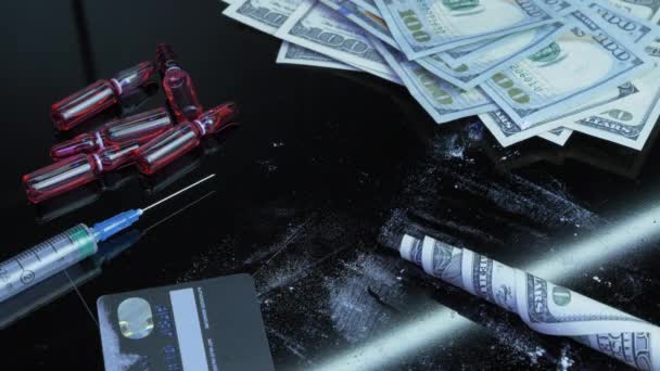 Detailní záběr srolované bankovky v amerických dolarech za drogou za použití černého pozadí s hotovostními penězi, stříkačkami a omamnými látkami. Kokainový prášek s dolarovými bankovkami na černém skle. Užívání drog — Stock video