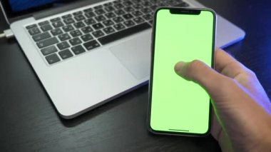 Erkek elinde boş dijital akıllı telefon. Adam ofiste oturuyor ve yeşil maket ekranlı telefon kullanıyor, internette sörf yapıyor, içerik videoları izliyor, haberleri kayıyor ve merkezi ekrana dokunuyor.