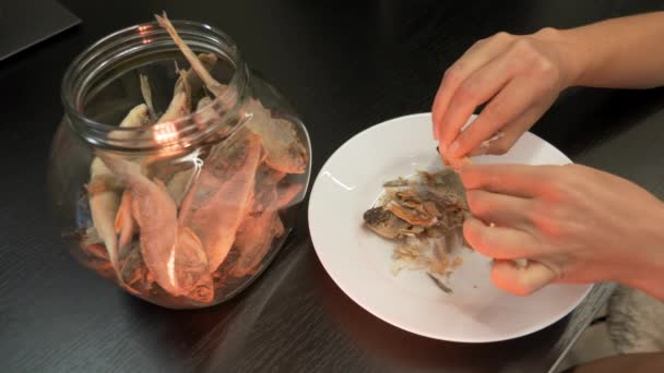 Mulher está comendo peixe seco na cozinha, de perto. A pessoa limpa e come peixe seco salgado durante a noite — Vídeo de Stock