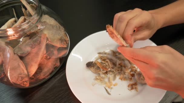 Le mani femminili puliscono il pesce asciugato salato di notte. Commestibile, pesca. Donna sta pulendo il pesce essiccato in cucina, da vicino — Video Stock