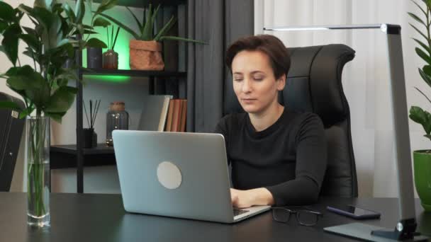 Focada mulher jovem concentrada está trabalhando no computador portátil no escritório elegante. Empresária está usando notebook em seu local de trabalho moderno. Feminino está digitando no teclado do laptop e olhando para a tela — Vídeo de Stock