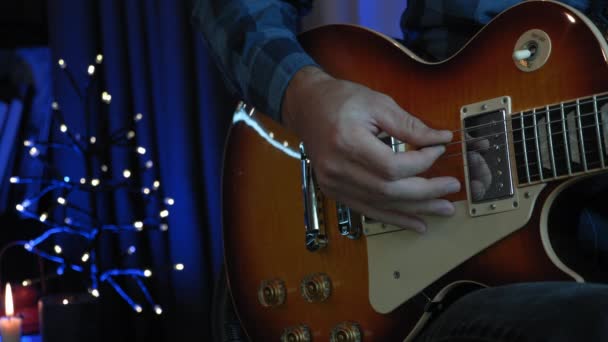 Férfi kéz játszik gitár húrok gitár pick sötét szobában homályos fények a háttérben, közelről. A zenész új akkordokat tanul elektromos gitáron. A gitáros szólóban játszik. — Stock videók