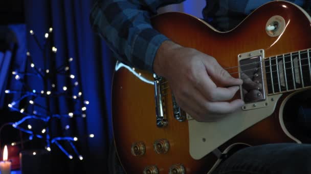 Férfi kéz játszik gitár húrok gitár csákány, közelről. Gitáros játszik elektromos gitáron sötét szobában homályos fények a háttérben. Zenei koncepció — Stock videók