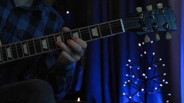 Professionele gitarist is akoestische gitaar aan het spelen in een donkere knusse kamer. Man 's hand met gitaar hals, vingers op gitaar snaren, close-up. Man muzikant leert akkoorden en nieuwe liedjes — Stockvideo