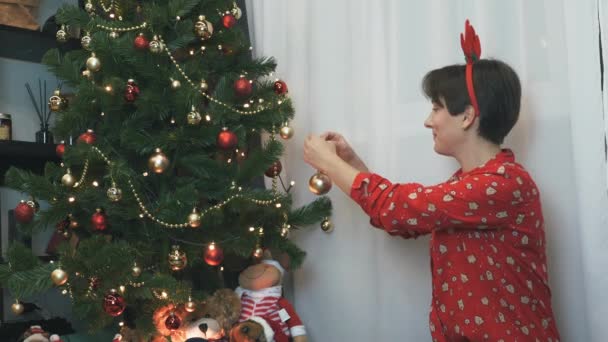 Feliz mujer encantadora está colgando de la bola en un árbol de Navidad, la decoración de árbol de Navidad, la preparación para el año nuevo 2021, un montón de regalos bajo el árbol. Feliz concepto de Navidad. Espíritu de vacaciones de invierno — Vídeo de stock