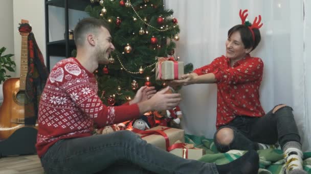 El hombre está emocionado de abrir regalo de regalo para Navidad. Hombre está disfrutando de la celebración festiva de vacaciones con la familia en casa. La mujer está dando caja de regalo en papel de regalo con lazo rojo. Feliz concepto de Navidad — Vídeo de stock