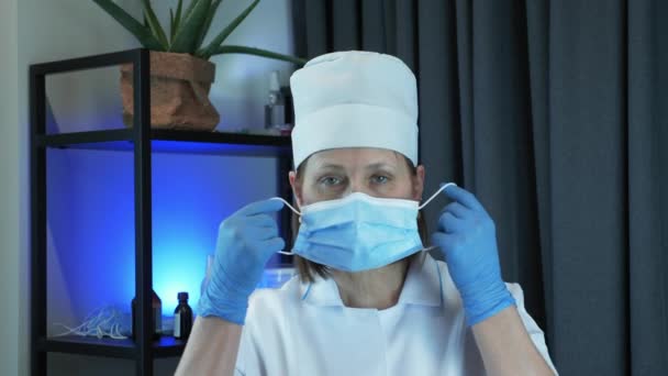 Femme médecin ou infirmière en tenue médicale de protection met sur masque médical dans le bureau du laboratoire de recherche. Portrait de femme met un masque médical pour la prévention et la protection des infections virales — Video