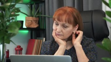 Düşünceli kadın iş yerinde dizüstü bilgisayarla oturuyor. Düşünceli iş kadını ofiste masa başı düşünüyor. Odaklanmış kadın, işteki sorunları düşünmekten başka bir şey yapmıyor.