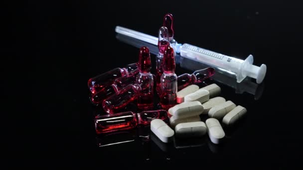 White pills, medicine ampoules with red vaccine, drugs or narcotics and syringe on black background, close up. Healthcare and drugs addiction concept — Stock Video