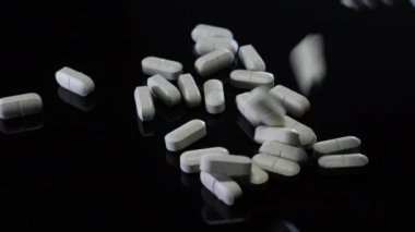 Tıbbi beyaz haplar siyah arka plana dökülüyor. Tabletler masanın üzerine düşüyor. Uyuşturucu bağımlılığı, ilaç endüstrisi konsepti. Tıp konsepti