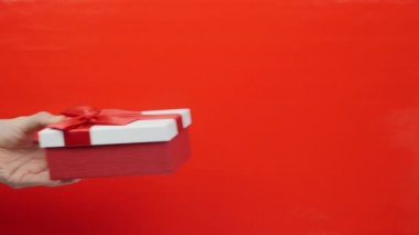 El, kırmızı arka planda kırmızı kurdeleli hediye paketi veriyor. Erkek, sevgililer gününde, Noel 'de ya da doğum gününde kadınlara hediye kutusu verir. Tatil hediyesi