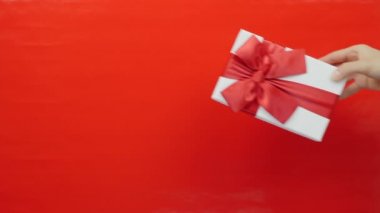 Kırmızı arka planda Sevgililer Günü hediyesi. Doğum günü, Noel ya da Sevgililer Günü için kırmızı kurdeleli hediye kutusu. Kadın eli, erkek eline hediye verir, yakın çekim.