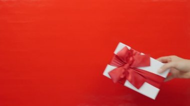 Kadın eli kırmızı arka plandaki adama hediye kutusunu veriyor. Sevgililer Günü ya da doğum günü hediyesi. Sevgililer Günü için kırmızı kurdele ile sarılı hediye kutusu, 14 Şubat, sevgili insanlara